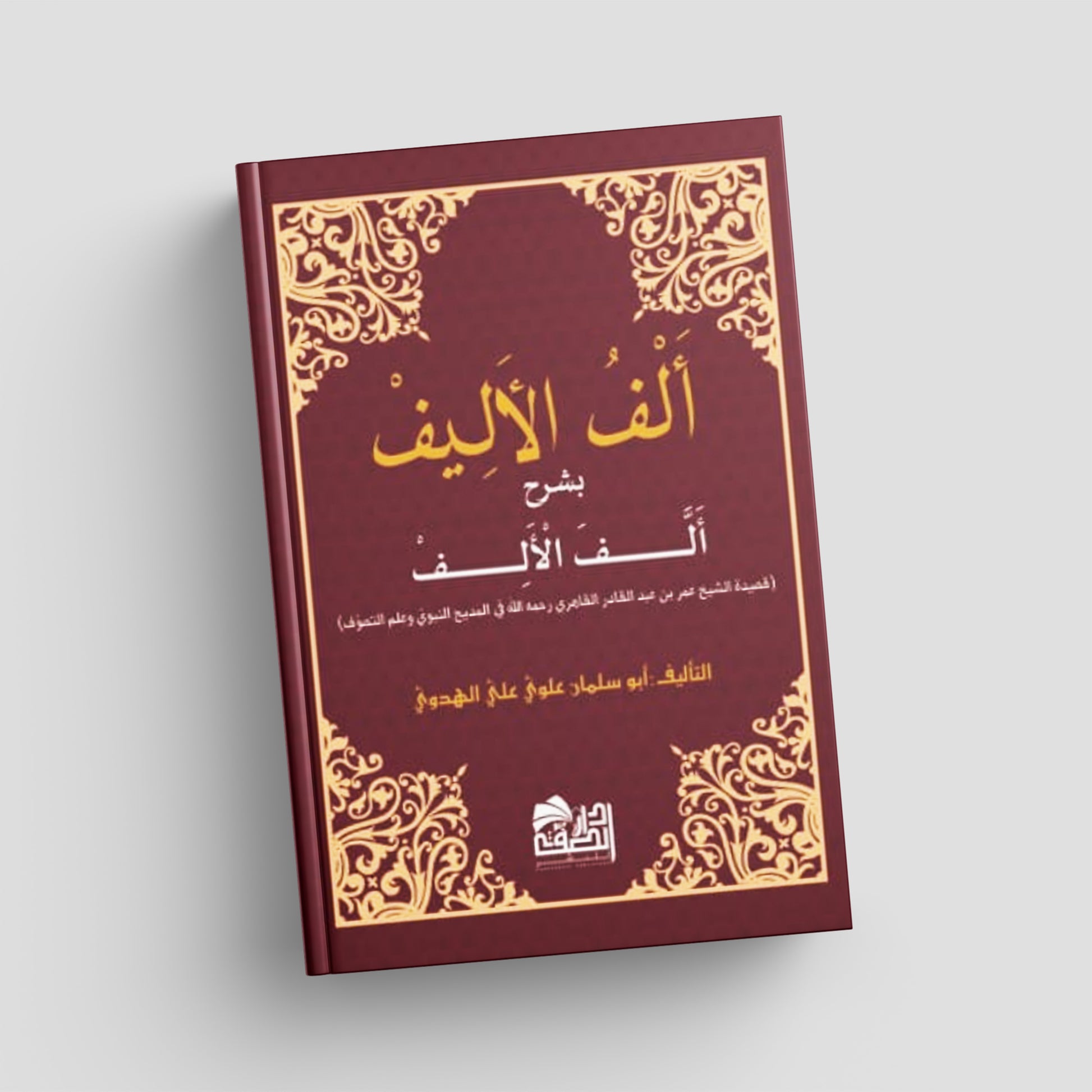 Maroon book with gold Arabic text and design on a light gray background